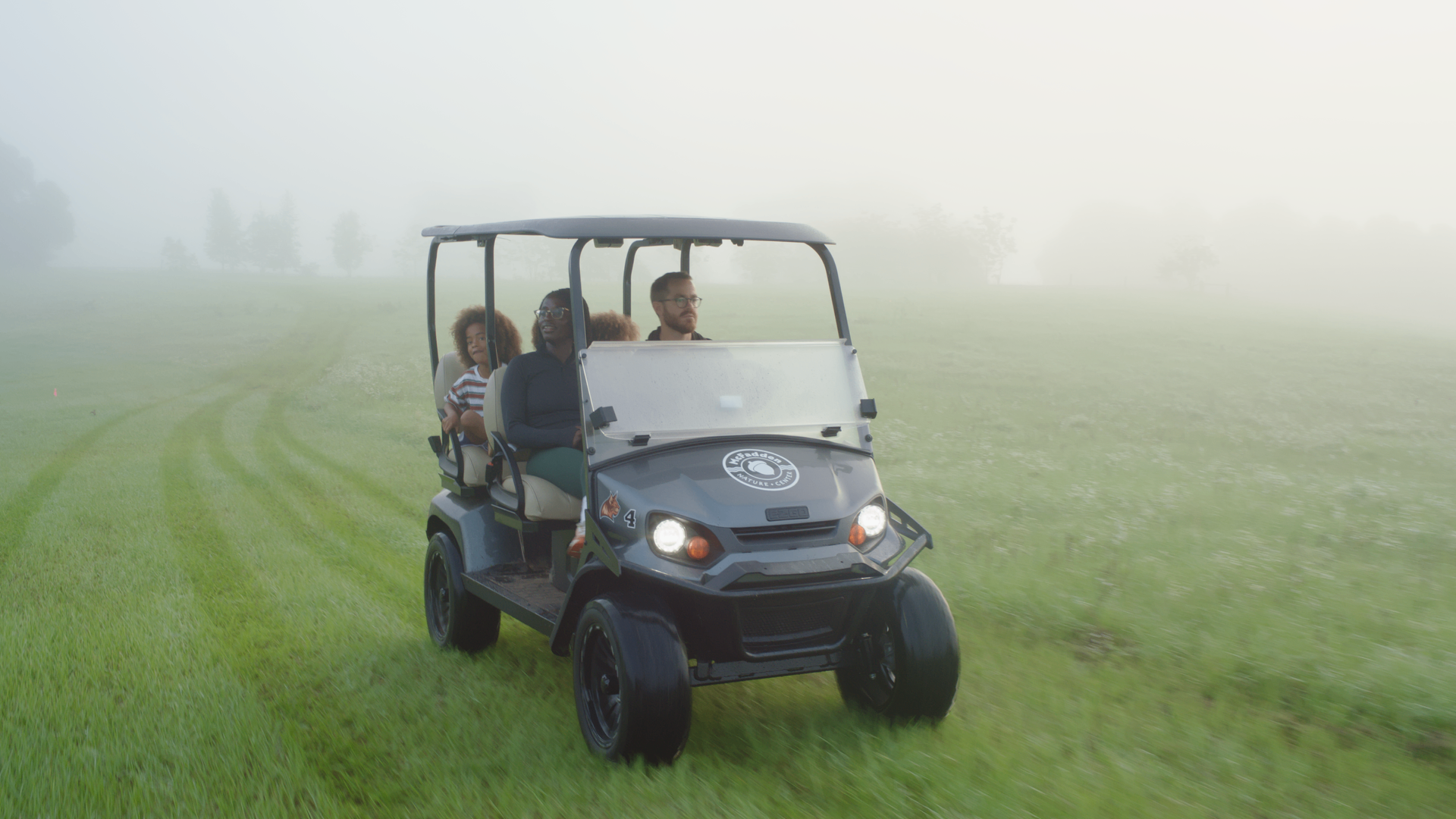 A family riding a golf cart through a beautiful misty green field at McFadden Nature Center